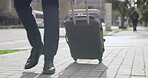 Closeup of male corporate executive pulling suitcase, walking to the city airport terminal to travel for a business trip. Formal entrepreneur crossing the street with luggage headed to hotel or home.