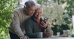 Happy, loving and mature old couple in love on phone video call outdoors in nature home garden. Smiling husband hugging and kissing wife while they laugh at funny graphic or meme on social media.