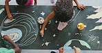 Young creative children drawing and making a colorful picture of space with chalk on a blackboard. Above view of kids coloring planets and stars. Artistic students doing a fun learning activity.