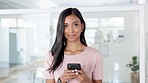 Closeup portrait of a young, happy and smiling black woman texting on her phone in a white modern office. Beautiful and attractive female chatting on a cellphone and looking directly into the camera