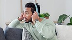 Listening, enjoying and streaming music online on a phone indoors by a young male. Modern, happy and relaxed man with headphones listen to internet radio or playlist at home at home on a sofa
