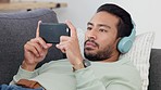 Young man jumps from fright over watching a horror movie or tv show on his phone at home, lying on his living room sofa. Surprised male enjoying online entertainment with streaming on demand services