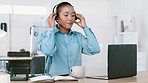 Happy black call center agent wearing a headset and working on a laptop in a modern office. Young African American woman talking on a video conference. Female smiling while working in customer care