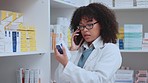 Pharmacist on a phone call talking, chatting and explaining medicine while reading box of medication, pills, or tablets inside a pharmacy. Busy female medical professional working alone in drug store