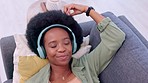 Trendy, funky and relaxed girl with headphones listening and enjoying music while relaxing on sofa at home. Cool young afro woman smiling to her favorite song and thinking about good time memories