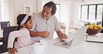 Foster parent and adopted daughter spending family time together, bonding at home and browsing on a laptop at home. Father and little girl sitting in the kitchen, surfing the internet and talking