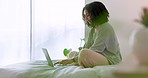 Laptop, bedroom and morning with a woman typing on a computer and sitting on a bed in her home. Author, writer or journalist working on a publication with the internet and wireless technology