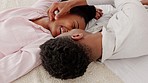 Happy, love and couple in a bedroom kiss and laughing in happiness, bonding time together at home. Young black man and woman kissing while lying on a bed with a smile in joy for caring relationship.