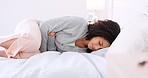 Period, menstruation and cramps with a woman in bed holding her stomach in pain in the bedroom of a home. Young female with a tummy cramp feeling sick, ill or unwell in her room in the house