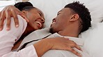 Happy, love and couple in a bedroom laughing and bonding while lying together at home. Young black man and woman  on a bed to relax and rest in a caring and joyful relationship during their honeymoon