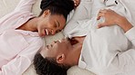 Black couple, love and bedroom moments while laughing and talking while lying together on bed at home from above. Black man and woman relax in pajamas in a caring relationship during honeymoon
