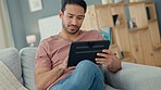 Man on a digital tablet winning a game online while sitting on a sofa in his living room at home. Happy and excited guy celebrating the victory of successful sport bet on the internet with technology