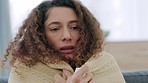 Sick woman suffering with covid symptoms, cold or flu while sitting on the couch at home. Worried female with anxiety about corona covering herself with a blanket, anxious, fraid and shivering 