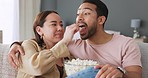 Couple in living room, eating popcorn and tv streaming comedy movie on home sofa together. Happy young love marriage, asian woman leisure time snack on couch and latino man smile watch youtube video