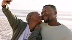 Happy black couple taking a phone selfie at the beach, kiss and bonding on a seaside getaway or trip outdoors. Young African American man and woman enjoying their freedom and relationship on holiday
