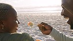 Happy black couple, sushi and beach laughing and eating in romance on a sandy shore. African man feeding his wife seafood in happiness, sharing and joyful laugh on a ocean coast outdoors by the sea