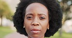 Face, head and hair with a black woman standing outside alone and looking at the camera with a blank expression. Portrait of a serious young African American female outdoor against a green background