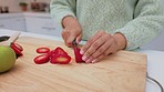 Hands, fruit and diet with a knife in the hand of a woman cutting a strawberry in the kitchen of her home. Food, health and nutrition with a female slicing strawberries on a chopping board in a house