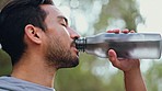 Man drinking water after workout and running outside, being healthy and hydrated. Portrait of male taking a sip of water from bottle after exercise in the park. Fitness, sports and training in nature