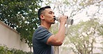 Drinking water, outdoor and man from China drink from a glass bottle near a road. Fit Chinese male person looking to hydrate with h2o to live a healthy lifestyle by green trees, grass and a car