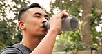 Drinking water, calm and outdoor man from China in nature feeling peace after hydrate drink. Person relax by trees and green plants sipping liquid from a plastic bottle after a fitness workout