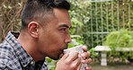 Thinking, serious and man drinking coffee while sitting in a backyard garden alone outdoor. Content, carefree and peaceful latin male relax and enjoying a cup or mug of tea while looking thoughtful