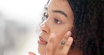 Skincare, beauty and apply face cream with a satisfied woman doing her morning routine for clear and moisturized skin in bathroom at home. Closeup face of curly hair girl using dermatology product