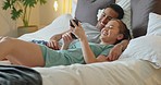 Asian couple, phone and social media for communication and entertainment on bed to relax, laughing and watch funny videp in bedroom at home. Man and woman using 5g internet while lying together