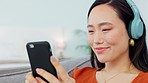 Asian woman, music headphones and smartphone social media app, podcast and audio ebook listening on living room sofa. Young girl face, mobile radio streaming and watch online technology at home 