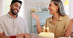 Birthday cake, couple and birthday celebration with a happy, excited and cheerful woman and man blowing candles at a table. Family, celebration and birthday party for interracial lady and guy at home