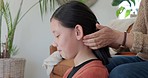 Asian, mother and hands tie hair of adolescent daughter at sofa in home living room. Family, youth and mama together with young teen in lounge of family home for hand braid hairstyle.

