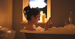 A young woman using her smartphone during a candlelit bath at night