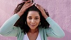 Portrait of a happy woman touching her afro while on an outdoor walk in the urban street. Closeup of Mexican girl fixing her hair and standing by pink wall in city while on summer vacation in Mexico.