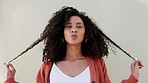 Beauty, hair and smile with a black woman being happy, playful and cute while standing on a gray background. Portrait of an attractive young female posing and playing with her curls by a wall