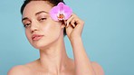 Face, flower and woman with skincare, natural beauty and wellness on blue studio background. Portrait, female, girl and plant for organic facial, eco friendly cosmetics and soft skin smooth and clear