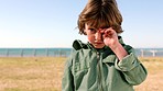 Travel, tired and face of child at beach exhausted at promenade on holiday in California, USA. Young caucasian boy on vacation at ocean sleepy standing on field in sunshine portrait.


