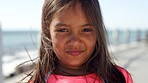 Child, face and wind in hair on a beach promenade for summer travel vacation outdoor for peace, calm and freedom. Portrait of a girl kid from the Philippines with a shy smile while on holiday at sea