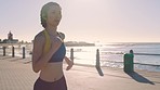 Woman, running and sunset at sea while outdoor for exercise, workout and cardio training for fitness while listening to music. Female runner at the beach promenade in Miami