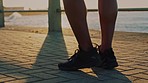 Fitness, shoes and man stretching feet for running on beach promenade, marathon and silhouette in sunshine outdoor. Closeup shadow of runner, sneakers and ready to start exercise on beach sidewalk 
