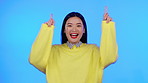 Asian woman, portrait and excited with hands for space, celebration or sale on a blue background. Happy model person pointing up for news announcement, promotion deal or competition winner in studio