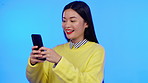 Asian woman, phone and studio for communication, internet and social media on a blue background. Happy model person on smartphone for online chat, meme or laughing at funny post on website in studio