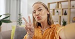 Selfie, home and face of a young gen z woman on a living room sofa with peace and emoji sign. Kiss, photo and portrait of a female on a lounge couch taking a image for social media profile picture