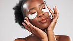 Face, skincare and black woman with eye patches in studio isolated on a gray background. Dermatology, beauty cosmetics and female model pose with facial collagen mask for healthy skin and anti aging.