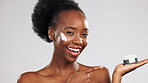 Face, skincare and black woman with cream container in studio isolated on a gray background. Dermatology portrait, cosmetics and happy female model laugh and pointing at lotion, creme or moisturizer.