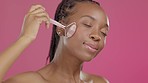 Skincare, massage and black woman with a jade roller on face isolated on a pink background in a studio. Beauty, relax and African girl with a product for facial wellness, treatment and relaxation