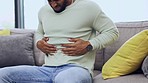 Man on a sofa with stomach pain, sickness or cramps while relaxing in the living room at his home. Medical emergency, illness and male with diarrhea, indigestion or food poisoning ache at his house.