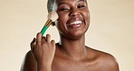 Beauty, makeup and black woman with a brush in a studio for a cosmetic, natural and face routine. Beautiful, happy and portrait of African model doing cosmetology facial treatment by brown background