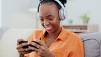 Phone games, headphones and black woman on couch gaming, online competition or esports mobile app. Young cyberpunk, gamer or person play internet video game on cellphone and electronics in her lounge