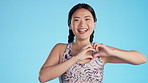 Asian woman, laughing or face with heart hands for support, wellness or cardiology healthcare on isolated blue background. Smile, happy or model portrait and love fingers, emoji shape or fashion sign