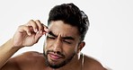 Man grooming his eyebrows with a tweezer in studio for self care, beauty and cleanliness. Hair removal, tweezing and male model from India doing facial epilation plucking routine by white background.